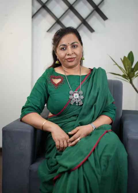 Neelam Chawlla in a green saree, seated in an armchair